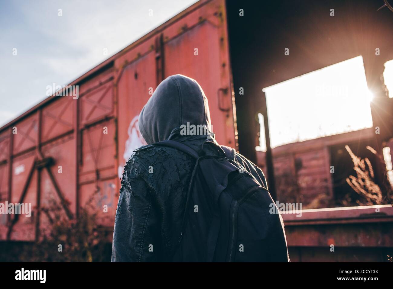 Inmigrantes sin hogar con hoodie caminando entre antiguos vagones de tren, el enfoque selectivo Foto de stock