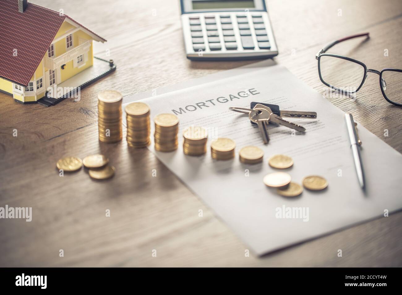 Contrato de hipoteca para la compra o venta de una casa de apartamentos o bienes raíces. Escritorio con monedas de contrato modelo casa calculadora y pluma Foto de stock