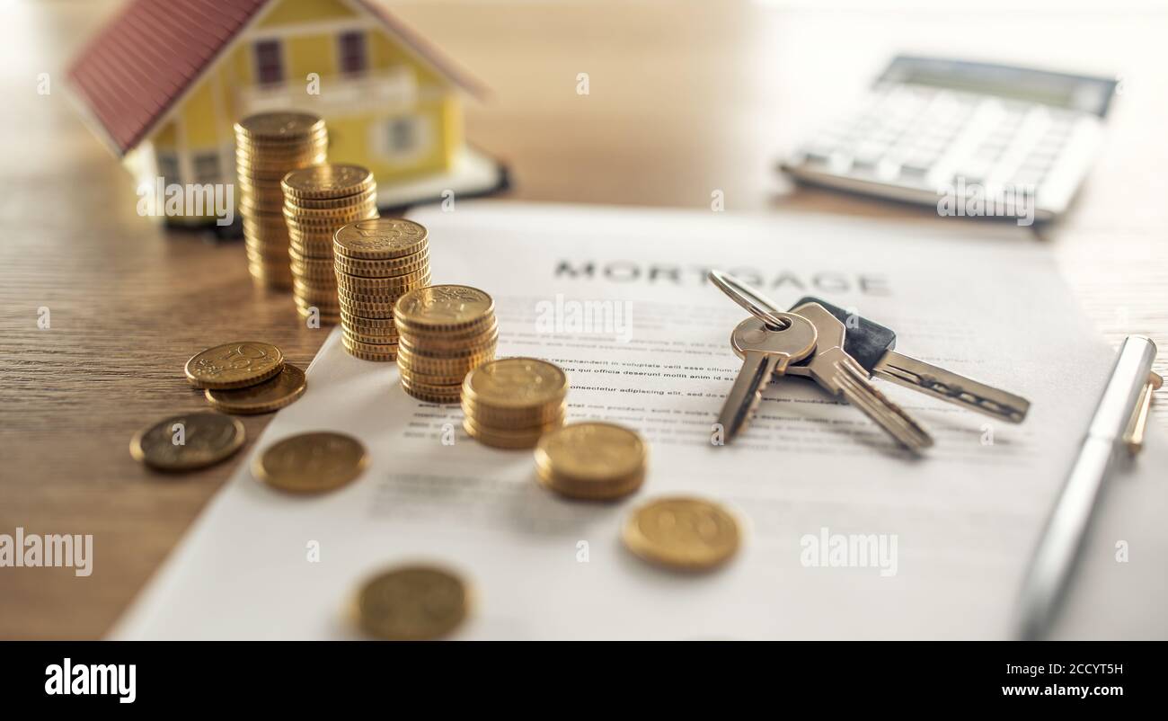 Contrato de hipoteca para la compra o venta de una casa de apartamentos o bienes raíces. Escritorio con monedas de contrato modelo casa calculadora y pluma Foto de stock