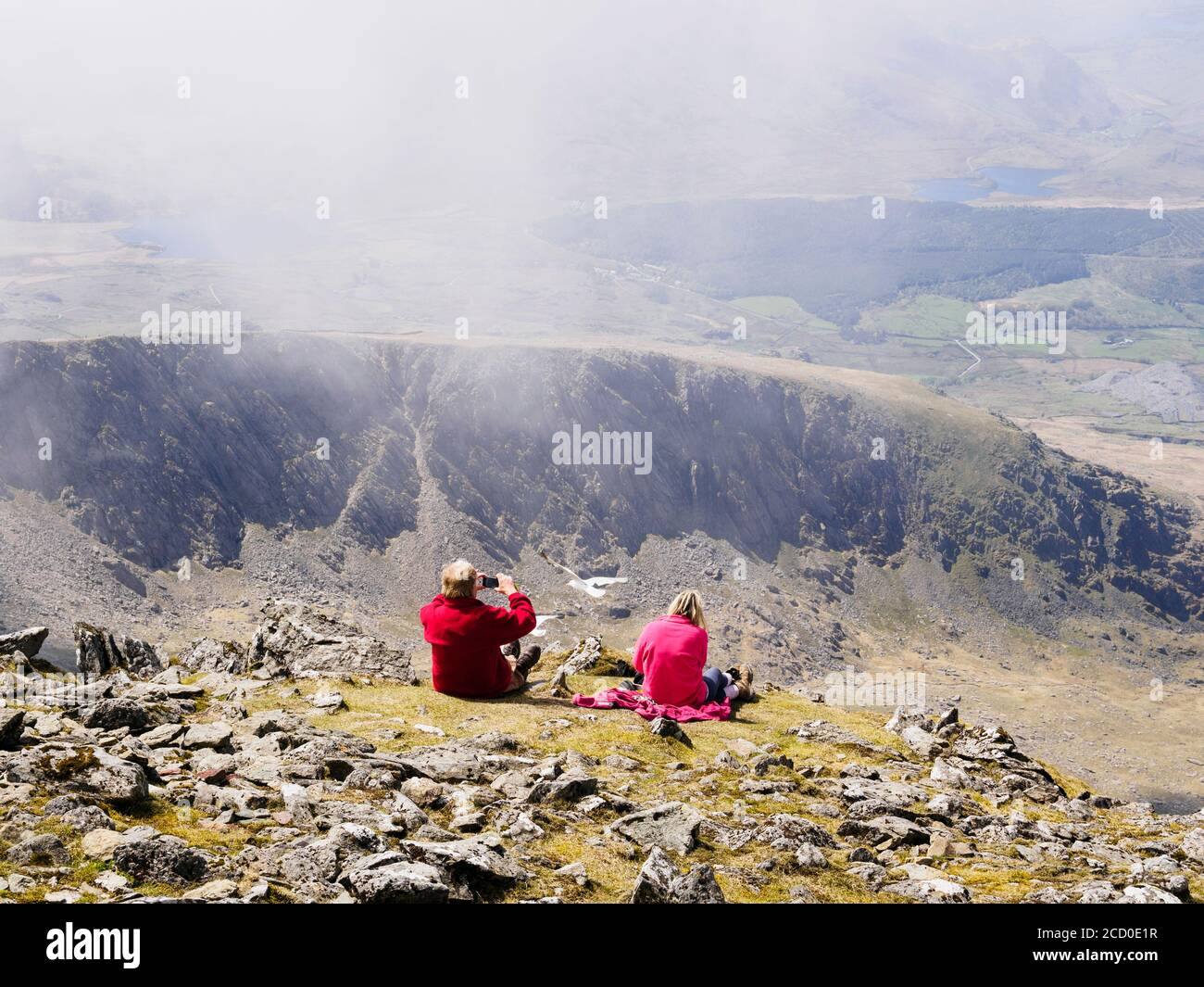 Dos personas descansando en el Monte Snowdon mirando hacia el sur a la cresta de Llechog en el Parque Nacional de Snowdonia, Gwynedd, Gales, Reino Unido, Gran Bretaña Foto de stock