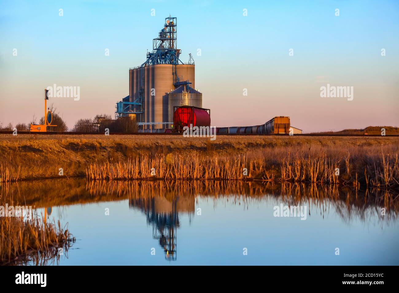 Instalación de almacenamiento de grano y tren en las praderas de Alberta reflejado en el agua; Alberta, Canadá Foto de stock