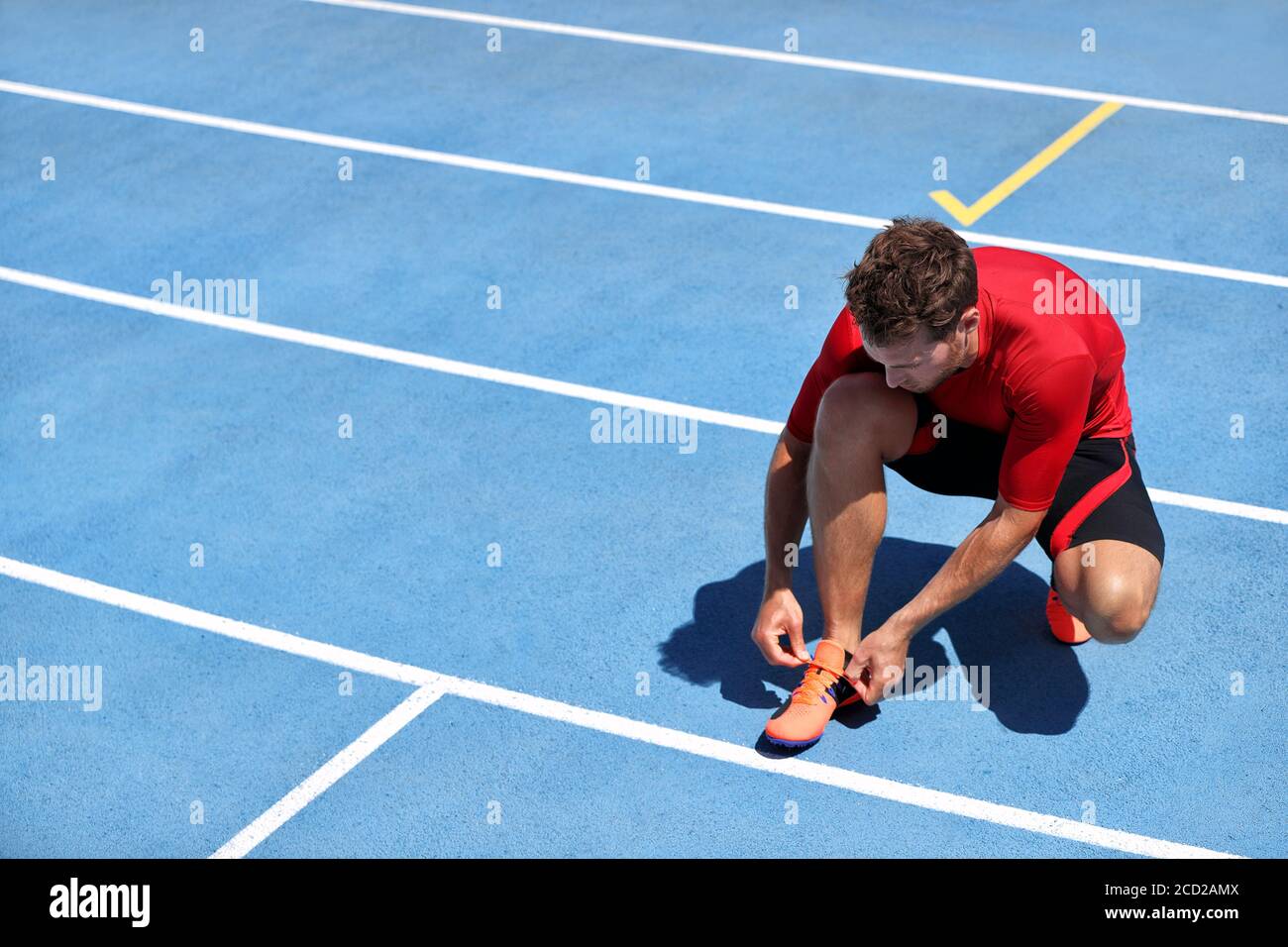 El atleta sprinter se prepara para correr atando cordones de zapatillas en  pistas de atletismo del estadio. Hombre corredor preparándose para la  carrera de entrenamiento de maratón al aire libre. Aptitud Fotografía