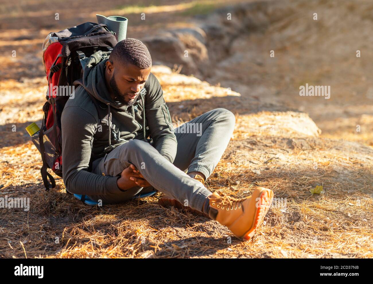 Hombre negro sentado en el suelo, frotándose la rodilla Foto de stock