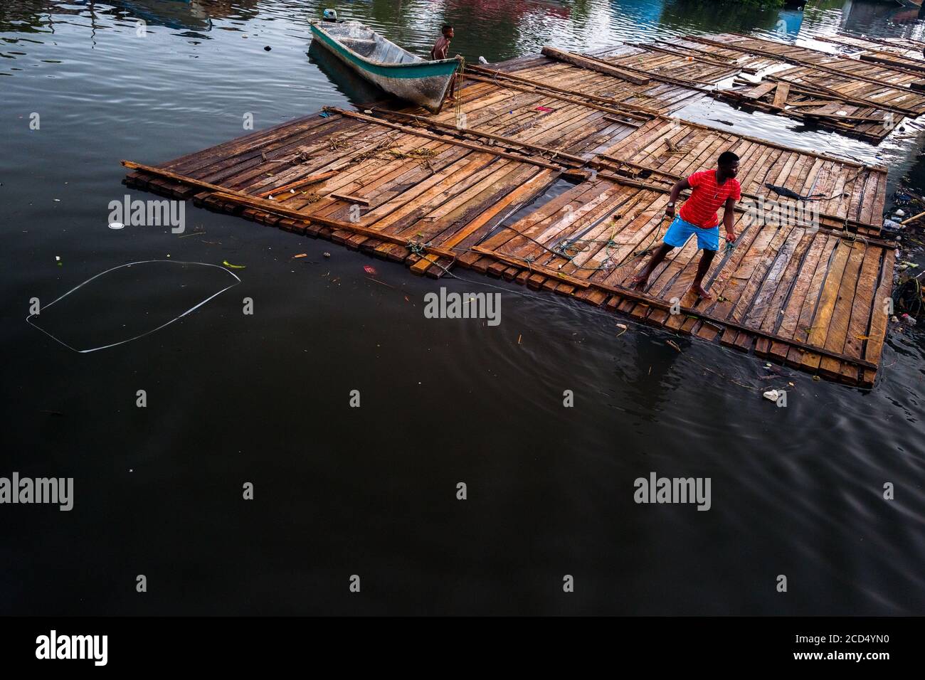 Un conductor de troncos colombiano está parado en una balsa de madera de  aserrado en bruto flotando en el agua durante el transporte de madera en el  puerto de Turbo, Colombia Fotografía