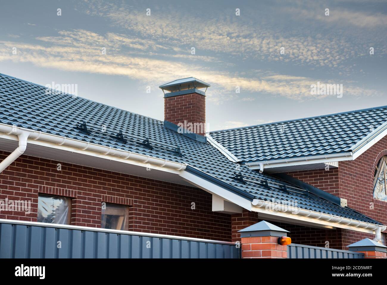 El nuevo marco de construcción alberga el sistema de canaleta de lluvia en la parte superior del techo de metal. Chimenea de ladrillo. Puertas metálicas automáticas. Foto de stock