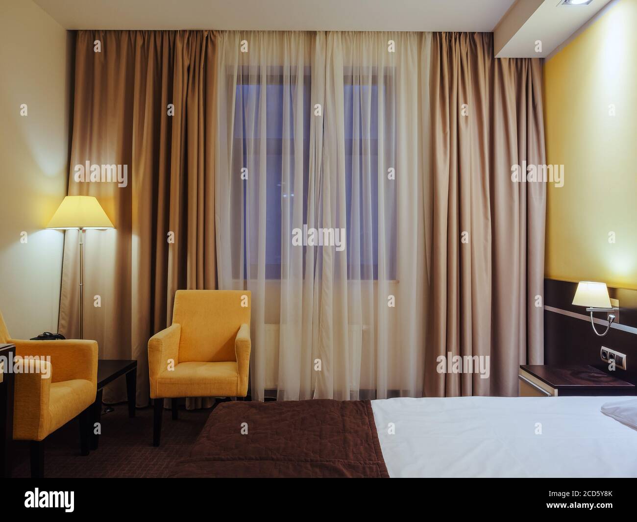 Sillones amarillos y una luminosa lámpara de pie en la esquina de la  habitación cerca de la ventana con cortinas. Interior de la habitación del  hotel Fotografía de stock - Alamy