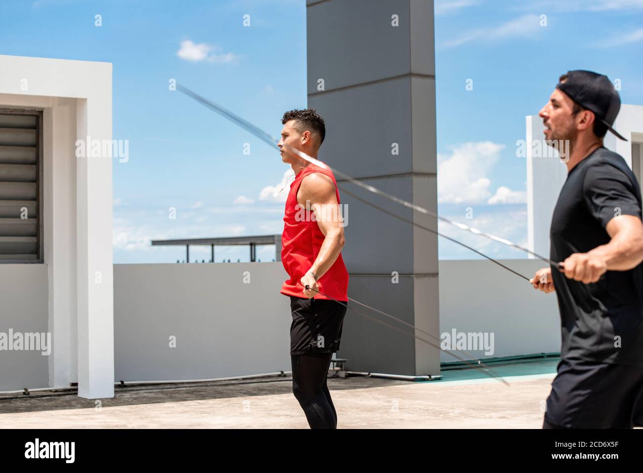 Dos deportistas caucásicos guapos haciendo ejercicio al aire libre por la mañana saltar cuerda en la azotea del edificio Foto de stock