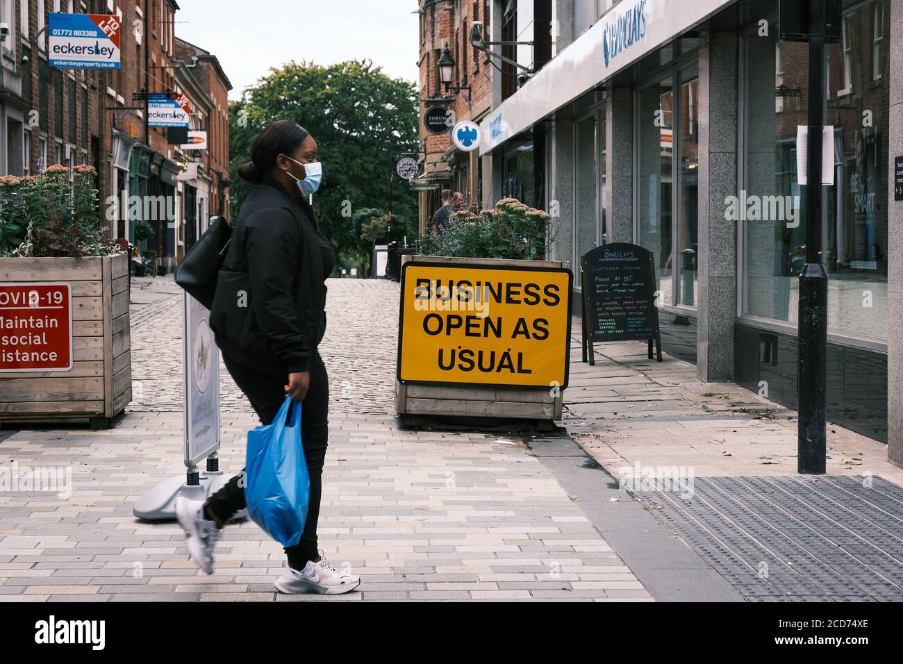 Mujeres negras en máscara con bolsa de compras caminando La principal calle comercial de Preson con 'Business Open AS Signo habitual en el fondo Foto de stock