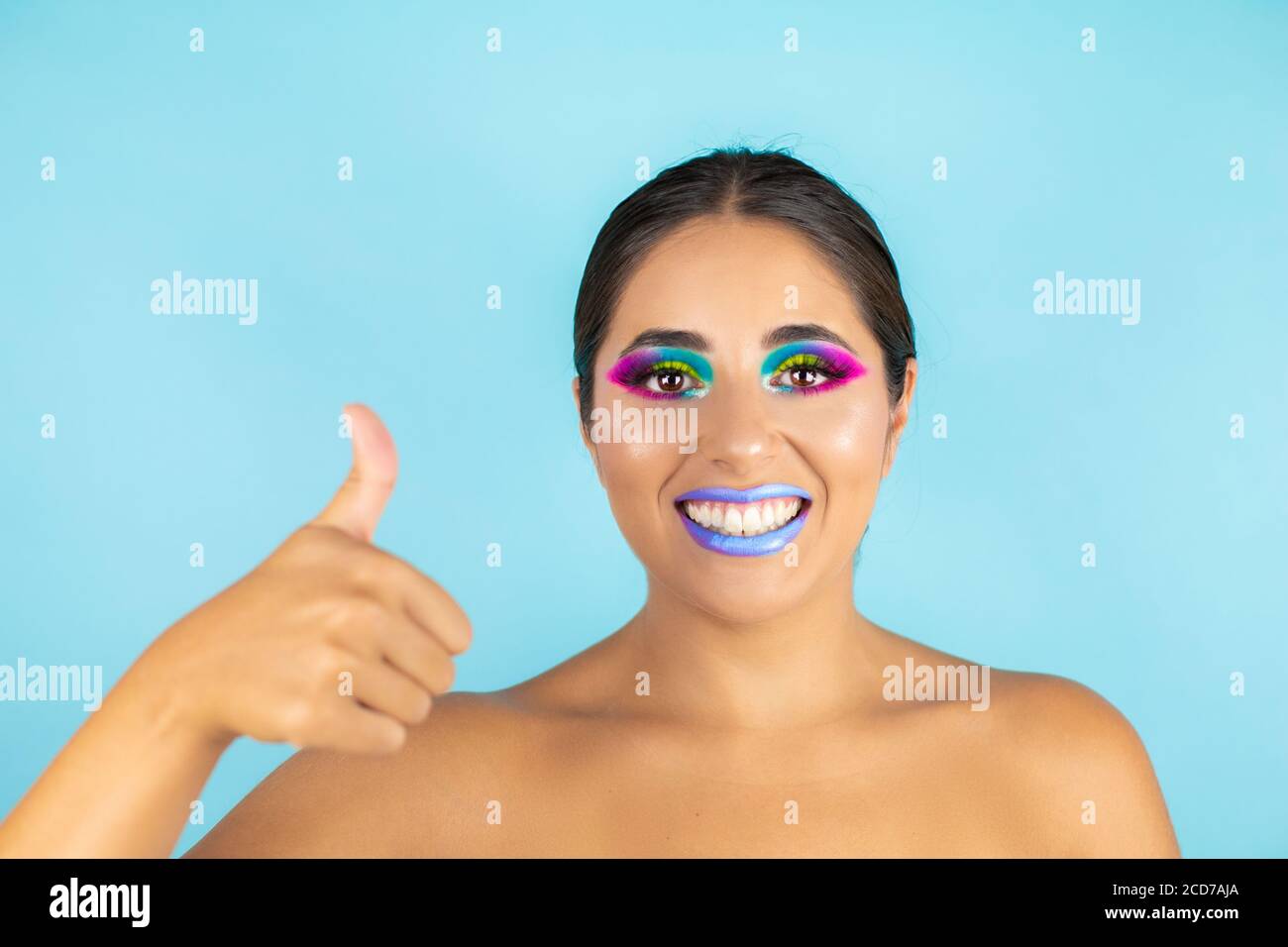 Retrato de belleza de modelo femenino con maquillaje vivo sobre fondo azul  y labios azules. Hacer un buen gesto con su pulgar Fotografía de stock -  Alamy