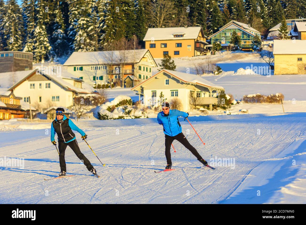 Dos esquiadores haciendo un ejercicio de patinaje a finales de la tarde de invierno cerca de un pueblo Foto de stock