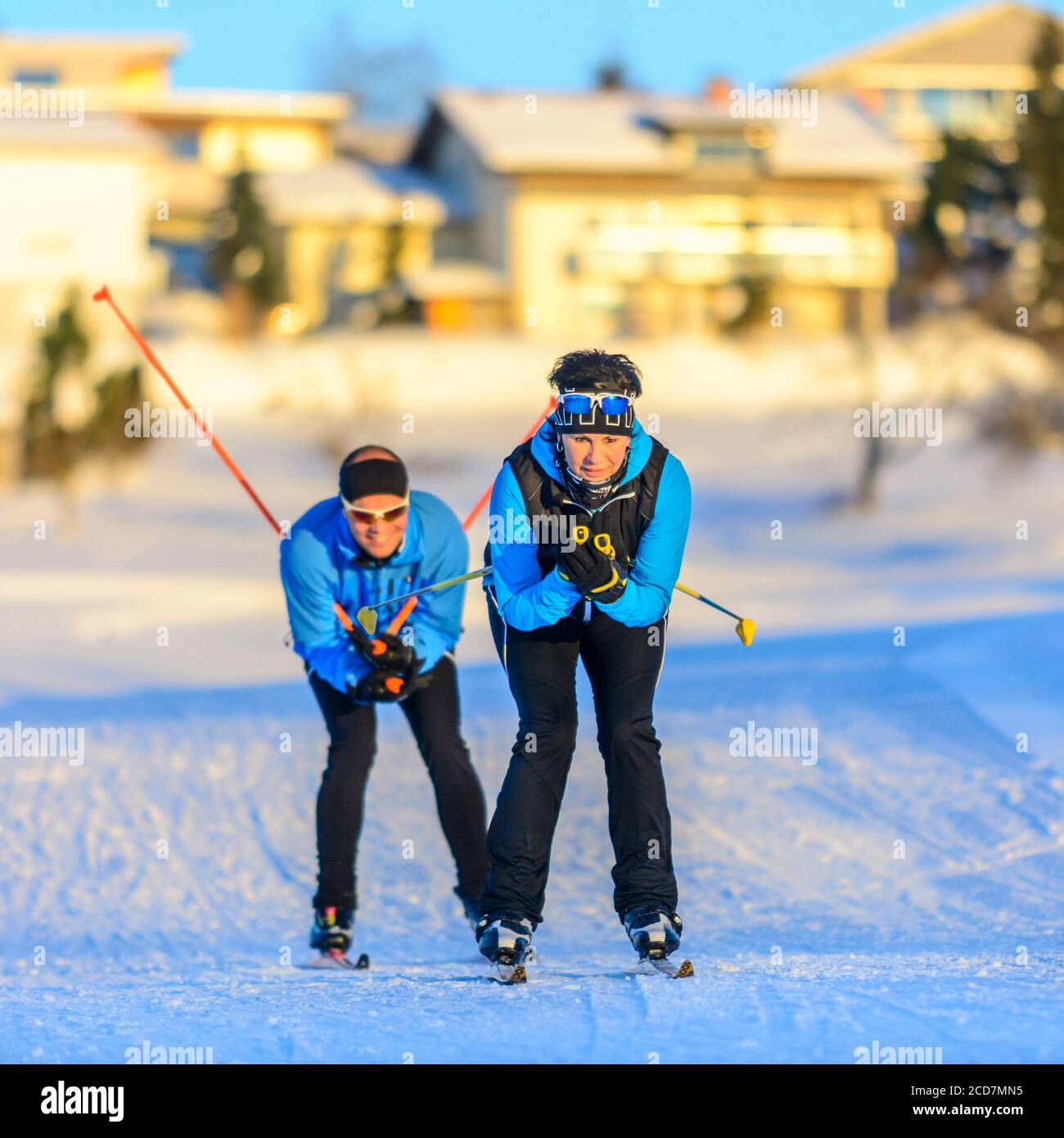 Dos esquiadores haciendo un ejercicio de patinaje a finales de la tarde de invierno cerca de un pueblo Foto de stock