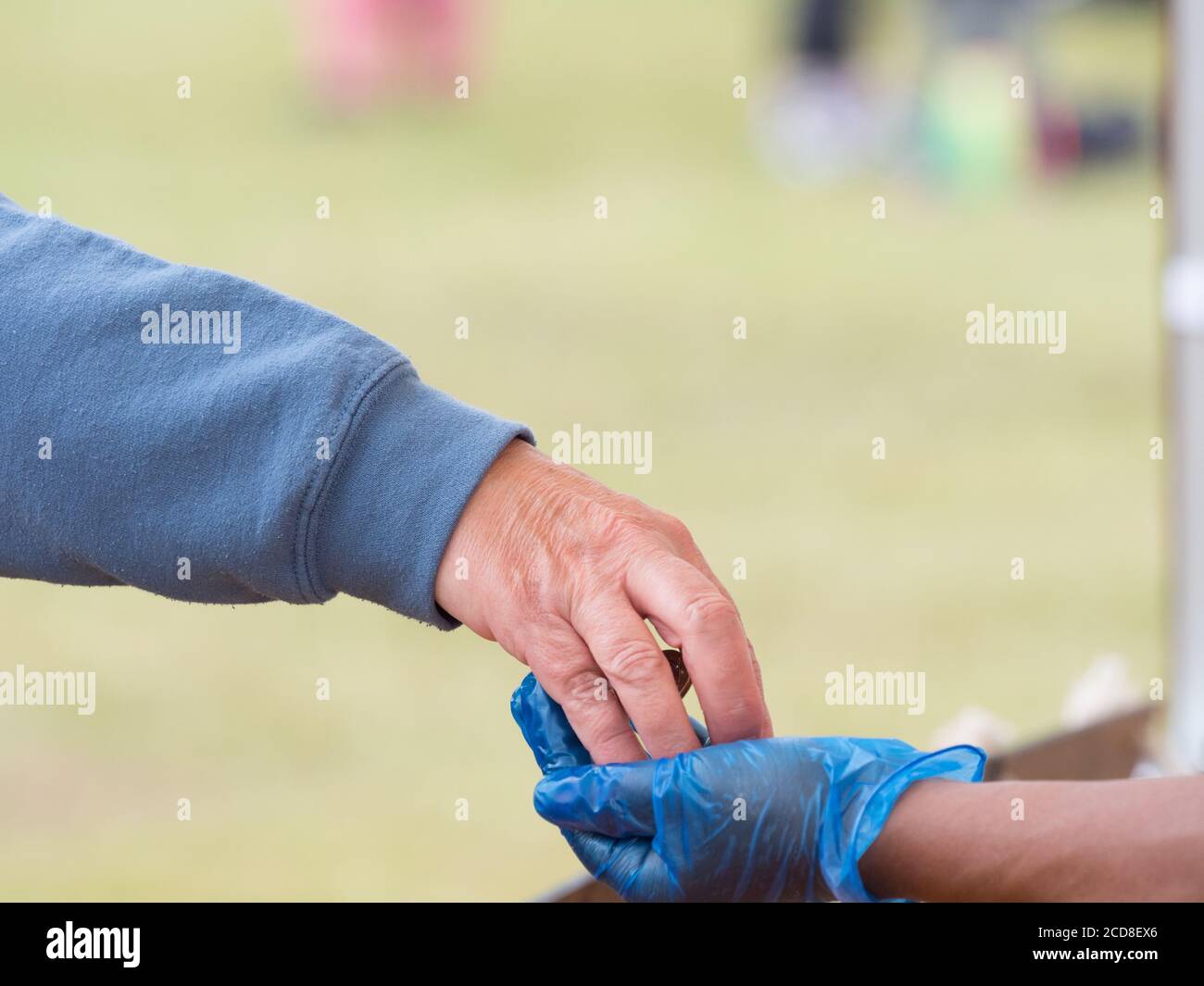 Una mano del cliente pone el dinero en una mano del sostenedor de la tienda usando un guante de higiene azul Foto de stock