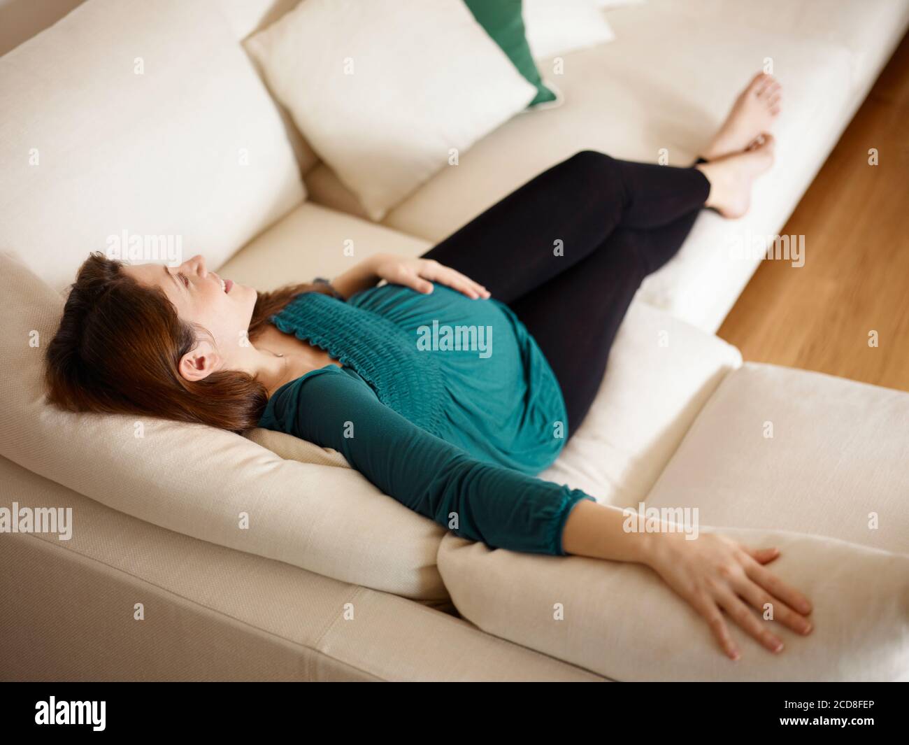 Joven embarazada Lying en el sofá y tocar el estómago Foto de stock