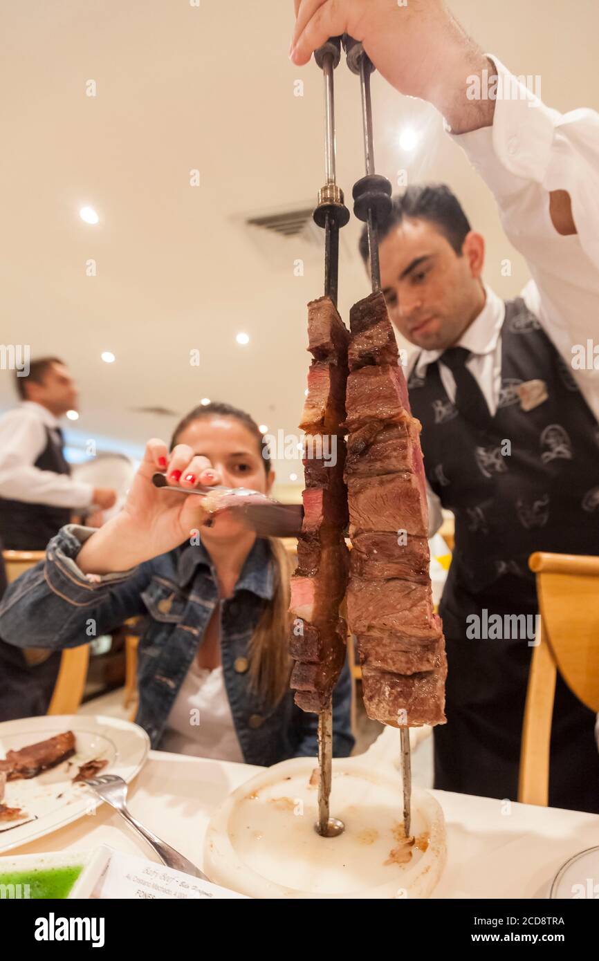 Brasil, estado de Minas Gerais, Belo Horizonte, restaurante Baby Beef, camarero que presenta brochetas de carne a un cliente Foto de stock