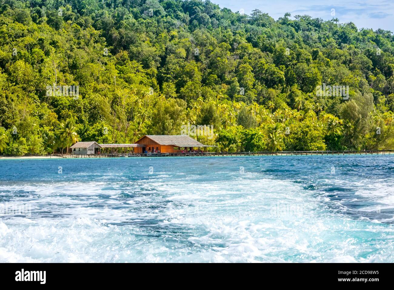 Isla tropical en Indonesia. Muelle de madera y cabaña en la orilla. Espuma de agua detrás de la popa del yate Foto de stock