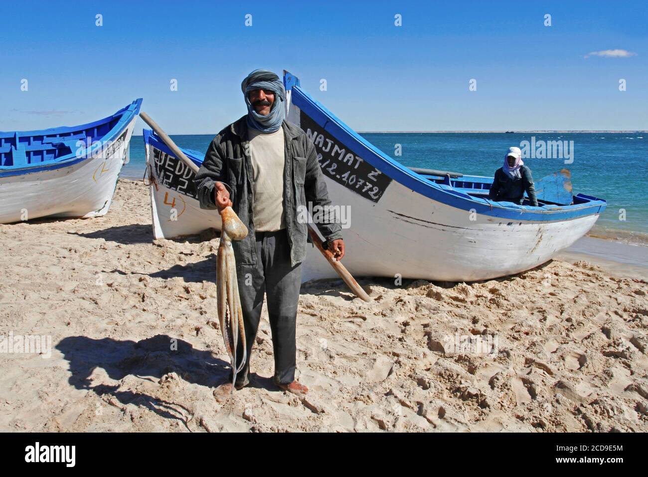 Marruecos, Sáhara Occidental, Dakhla, pescador con un pulpo en la mano frente a un barco en la playa Foto de stock