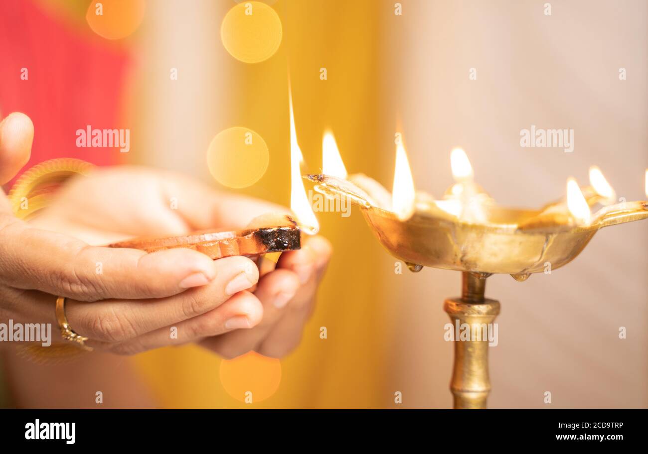 Cierre de manos de la mujer encendiendo linterna de aceite o diya durante la ceremonia del festival - concepto de festival tradicional indio y celebraciones rituales. Foto de stock