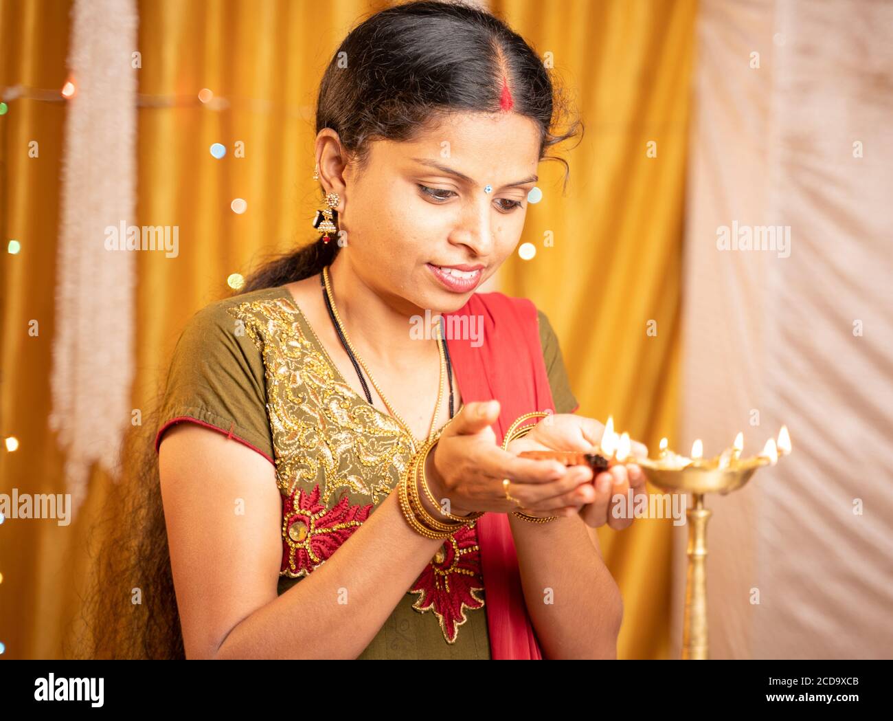 Feliz mujer India sonriente iluminación linterna o lámpara Diya durante la ceremonia del festival en casa - concepto de fiesta tradicional y celebraciones rituales. Foto de stock