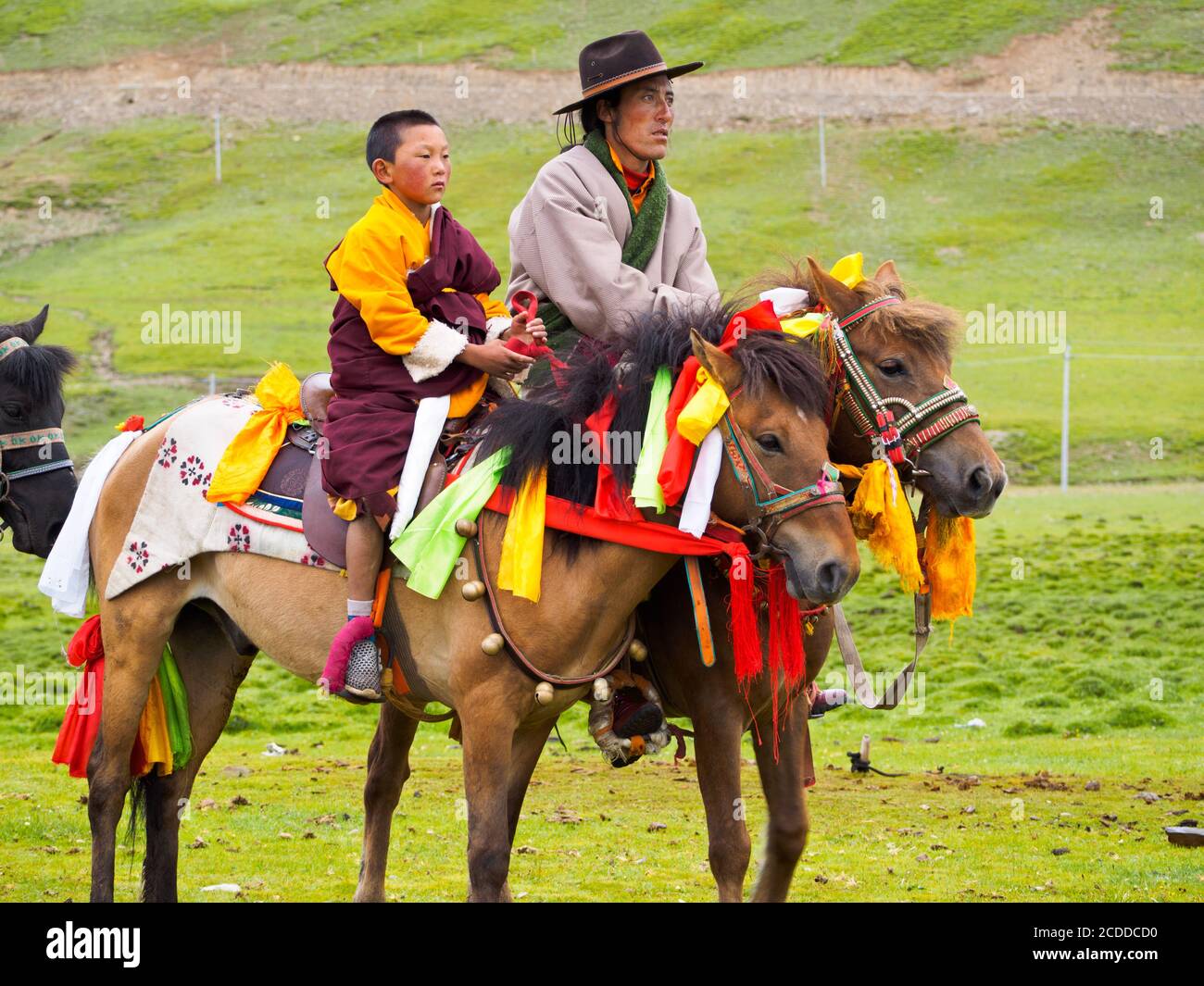 Un padre y un hijo en sus caballos esperando para ver las carreras de caballos en el festival de caballos cerca de la ciudad de Litang. Foto de stock