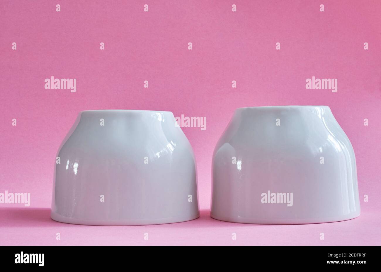 Dos tazas blancas de cerámica sin asas sobre un fondo rosa Foto de stock