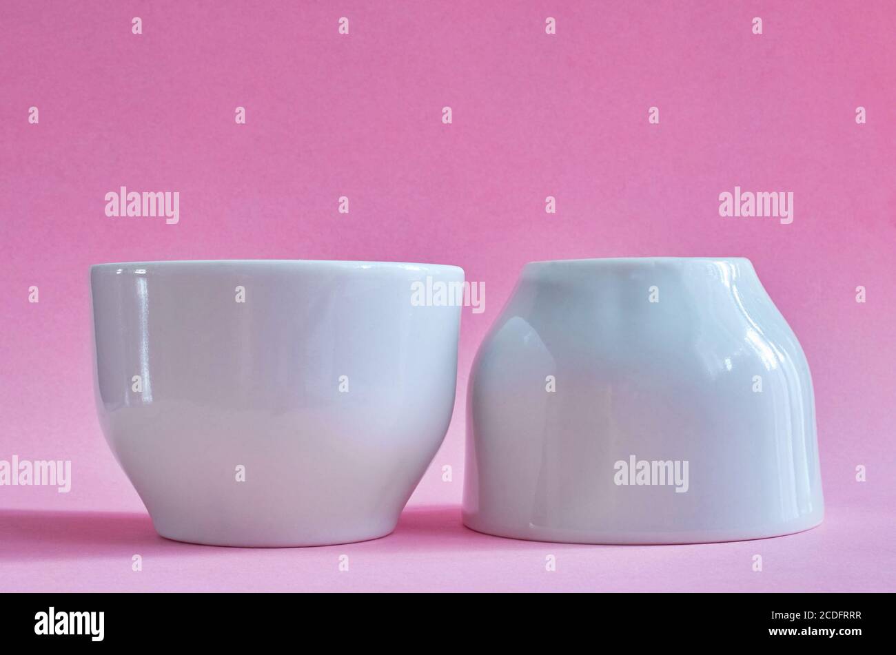 Dos tazas blancas de cerámica sin asas sobre un fondo rosa Foto de stock