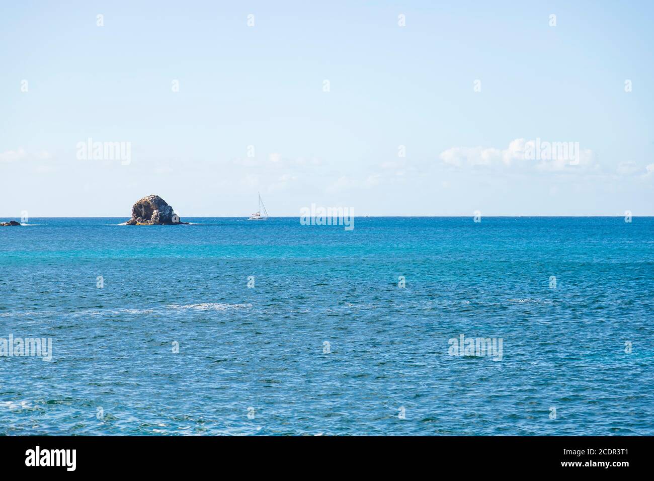 una forma terrestre oceánica aislada en el mar con un solo navegación de yates en el pasado en el fondo Foto de stock
