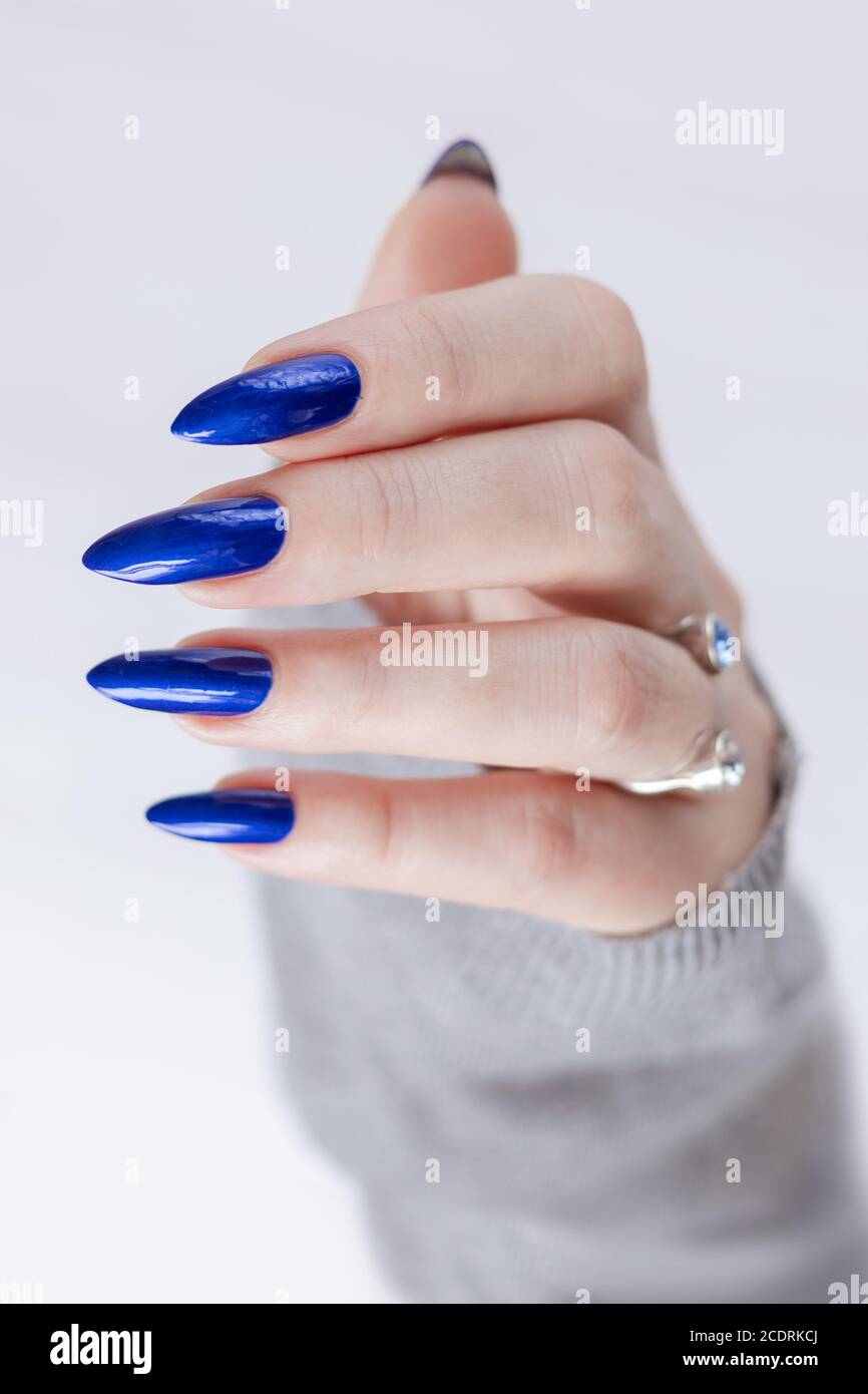 Mano femenina con uñas largas y manicura azul con botellas de esmalte de  uñas Fotografía de stock - Alamy