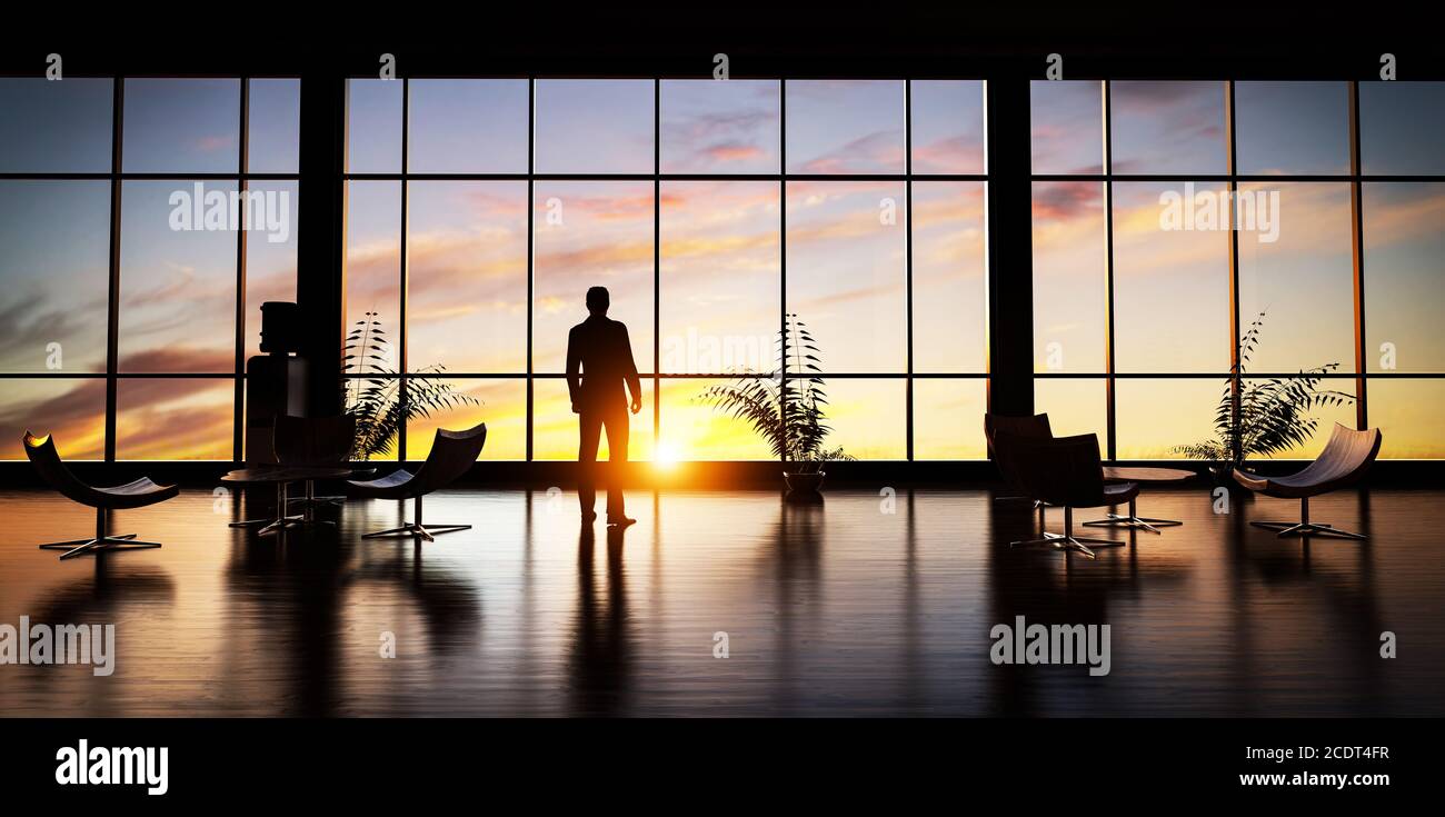 Hombre de negocios de pie en la oficina mirando por la ventana al cielo de la puesta de sol. Foto de stock