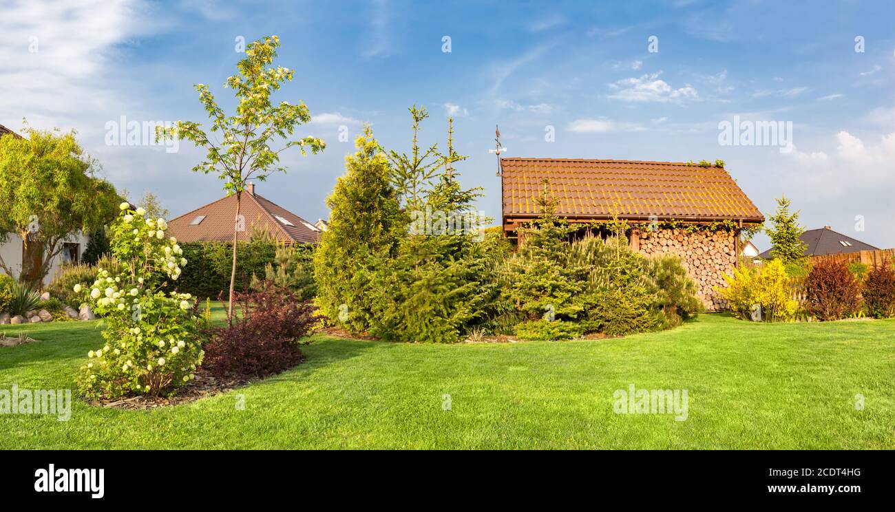 Patio trasero de una casa familiar. Jardín ajardinado con césped verde, refugio de madera. Foto de stock