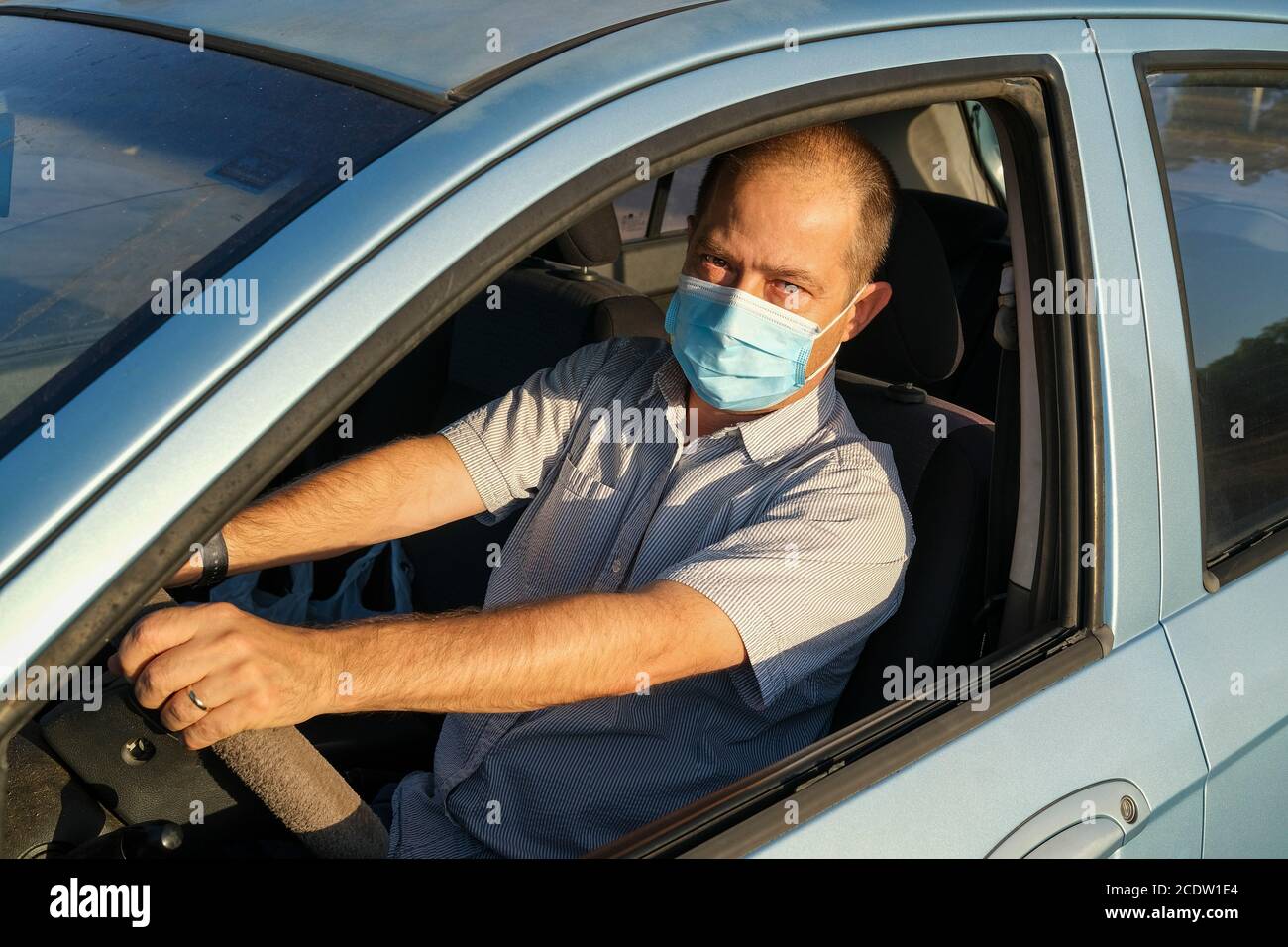 Hombre que lleva una máscara de papel quirúrgico en un coche Como prevención Covid19 Foto de stock