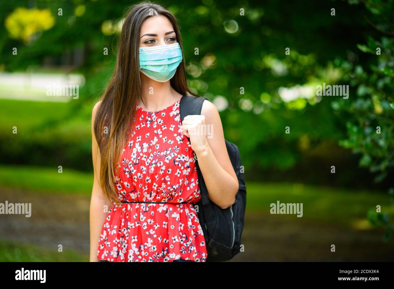 Estudiante que camina al aire libre en el parque y lleva una máscara para protegerse del coronavirus Foto de stock