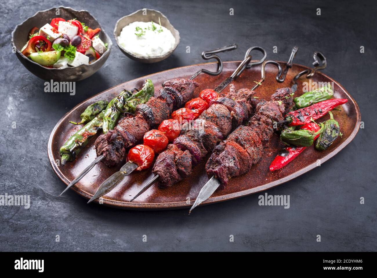 Shashlik ruso tradicional en una brocheta de barbacoa con ensalada de  granjero y tzatziki como closeup en una tabla de corte de madera Fotografía  de stock - Alamy