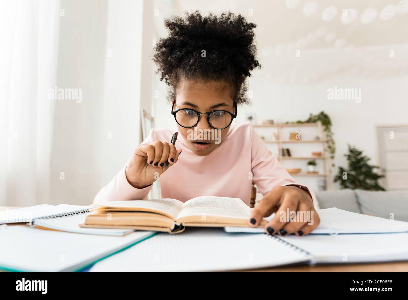 Libro de lectura de la muchacha adolescente africana sorprendida haciendo tareas en el hogar Foto de stock