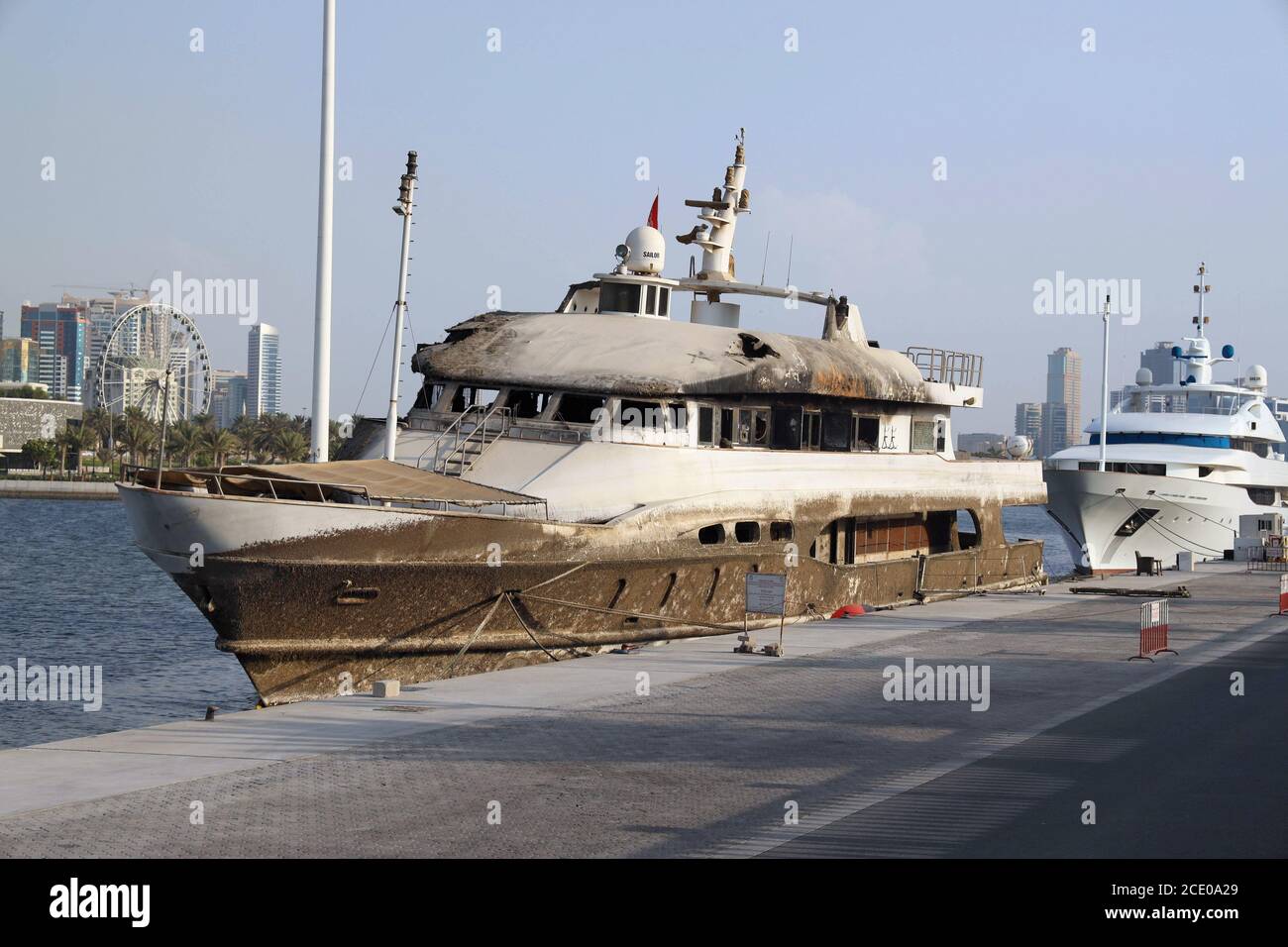 Un pequeño barco privado de acero quemado sin nombre comercial en contra El fondo de los rascacielos urbanos de Dubai Foto de stock