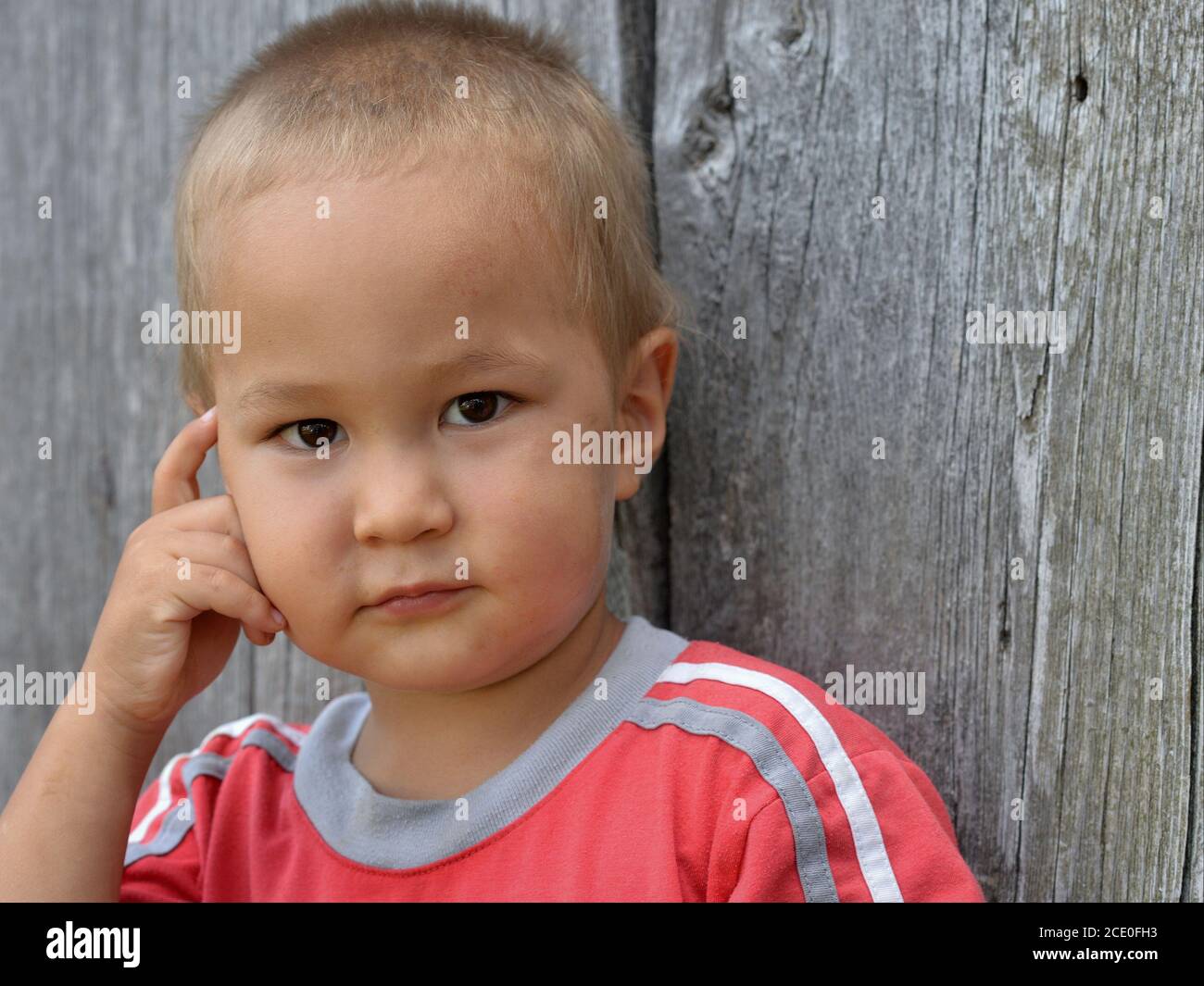 Lindo niño pequeño de raza mixta (caucásico y asiático oriental) posan para la cámara con su mano hacia su mejilla (postura pensante). Foto de stock