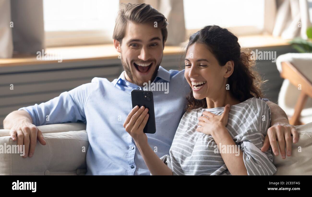 Emotivo joven pareja de alegría mirando la pantalla del smartphone. Foto de stock