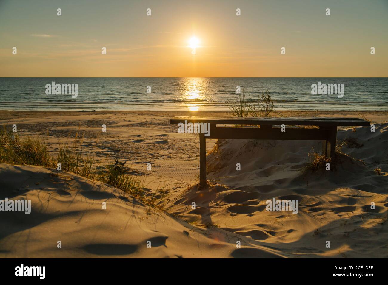 Banco vacío de madera y hermosa puesta de sol dorada en la playa. Puesta de sol en el mar en la noche tranquila. Nadie Foto de stock