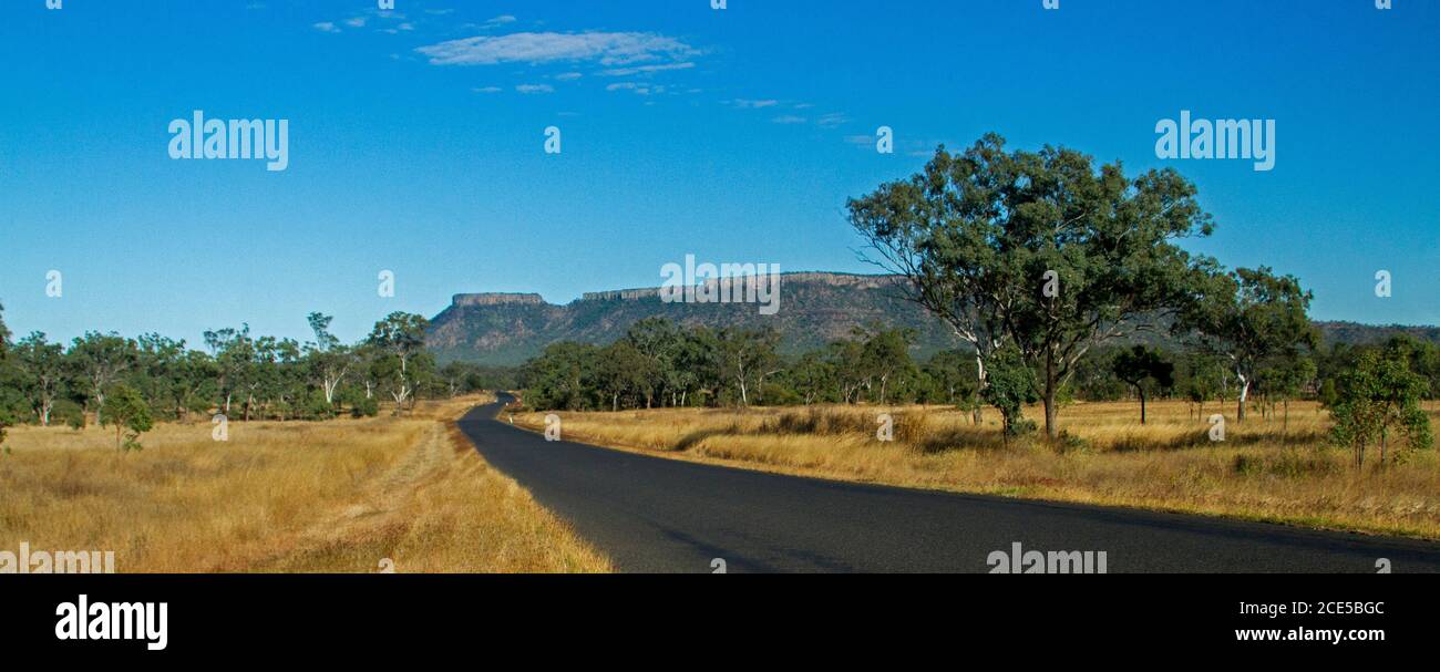 Vista panorámica de las colinas del Parque Nacional de Peak Range elevándose en el cielo azul con la carretera que serpentea a través del primer plano se encubró Los árboles en el Outback de Australia Foto de stock