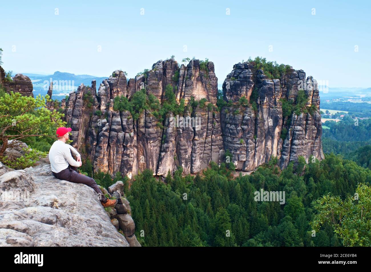 Hombre alto con gorra roja de béisbol sentado en el acantilado y observar las montañas. Silueta oscura de rocas. Foto de stock