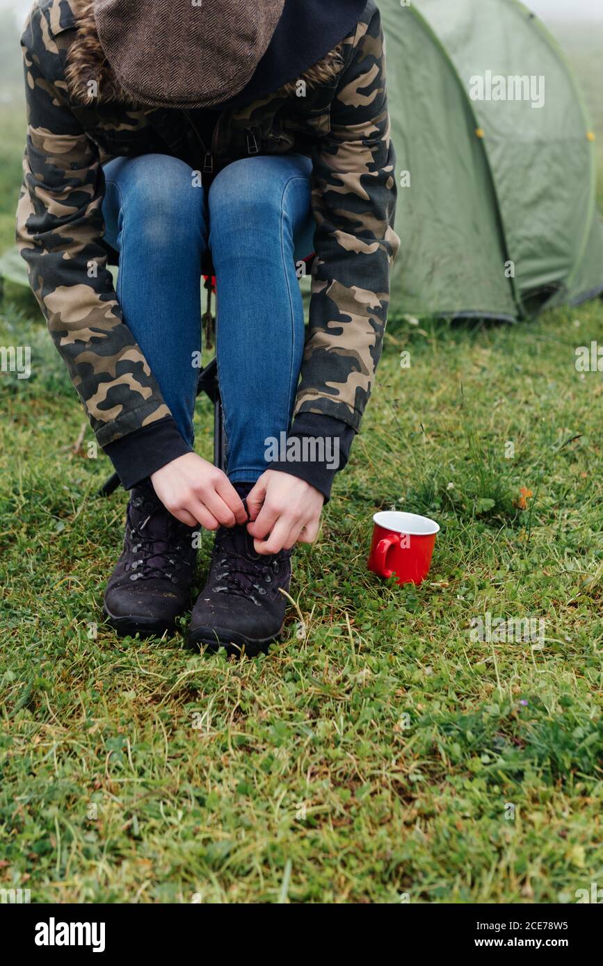 Gran ángulo de cosecha de hiker anónimo en el atado cálido de ropa exterior cordones de botas mientras descansa en el campamento Foto de stock