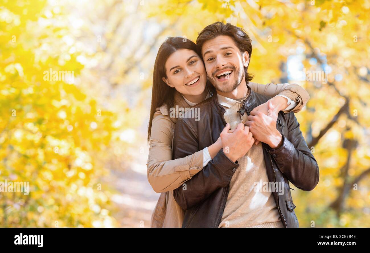 Mujer positiva abrazando a su hombre desde atrás, posando en el parque Foto de stock