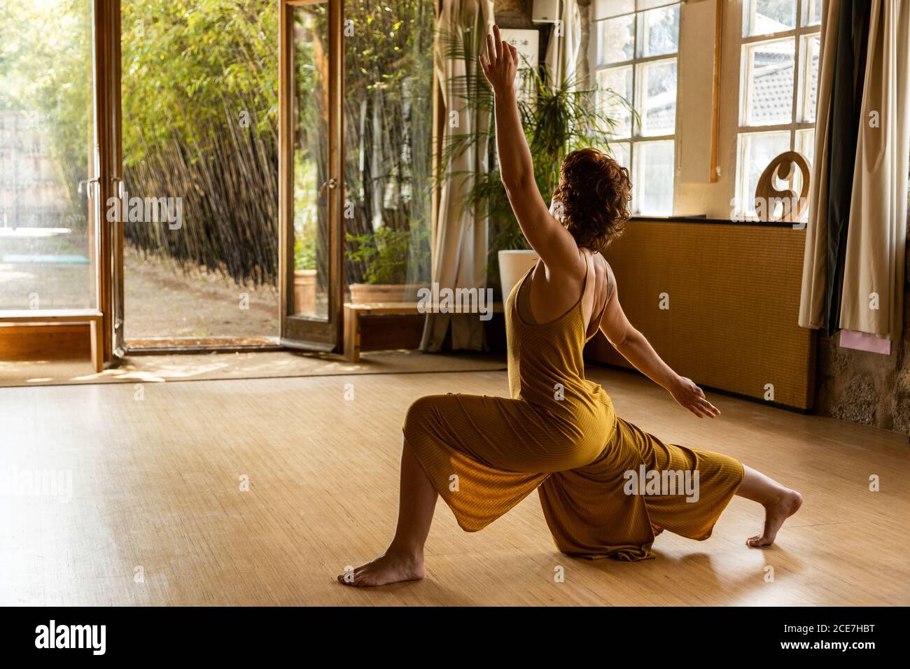Vista lateral de la mujer enfocada de pie descalzo en el estudio Anjaneyasana y haciendo yoga mientras se busca Foto de stock