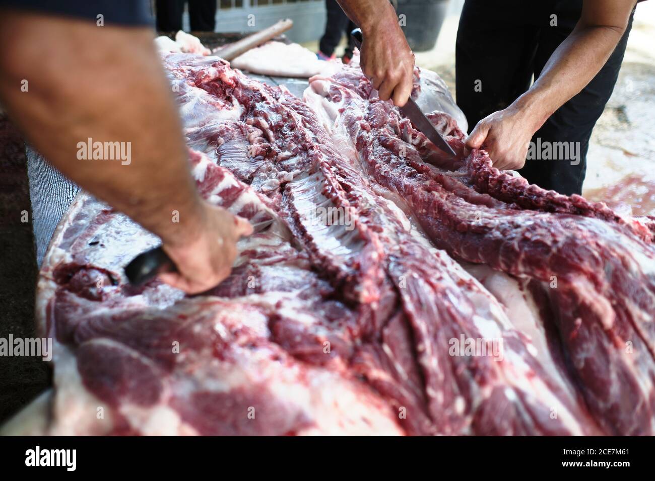 Gran ángulo de cultivo de carnicerías anónimas cortar carne de cerdo mesa de madera durante la producción de productos tradicionales en la granja Foto de stock