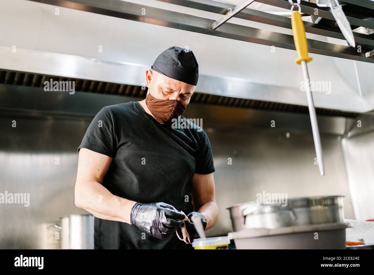 Cocinero masculino serio usando mascarilla de delantal y guantes de látex  preparándose la comida mientras trabaja en la cocina moderna del  restaurante Fotografía de stock - Alamy