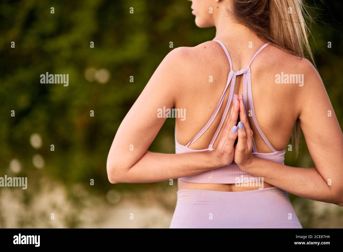 Unreconocible cosecha mujer en ropa deportiva practicando yoga con Namaste gesto detrás de la espalda y mirando lejos Foto de stock