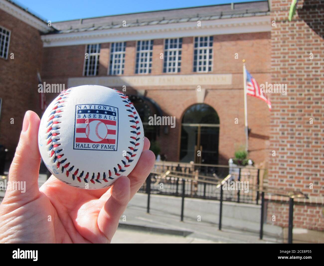 Cooperstown, NY / EE.UU. - 3 de junio de 2019: Un béisbol con el logotipo del Salón Nacional de la Fama del Béisbol frente al Museo del Salón Foto de stock