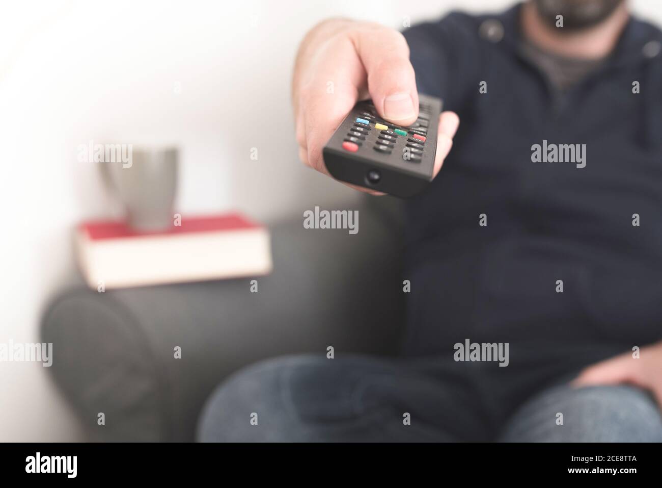 Vista frontal de la persona sentada en el sofá usando el mando a distancia de la televisión control para cambiar de canal Foto de stock