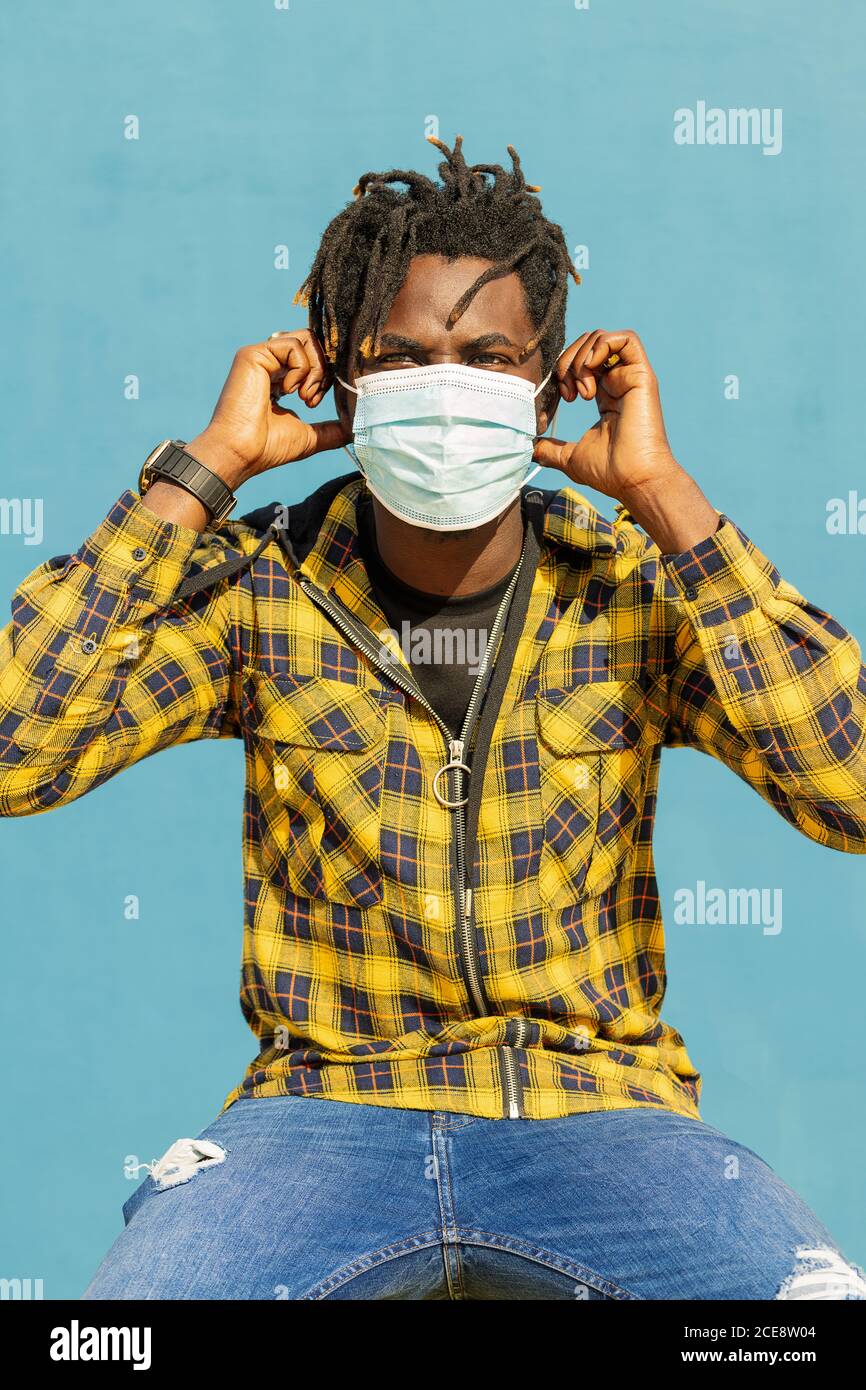 Chico joven guapo con estilo con una máscara protectora médica y gorra negra  en ropa de moda con una chaqueta y una sudadera con capucha en la calle.  moda y estilo urbano