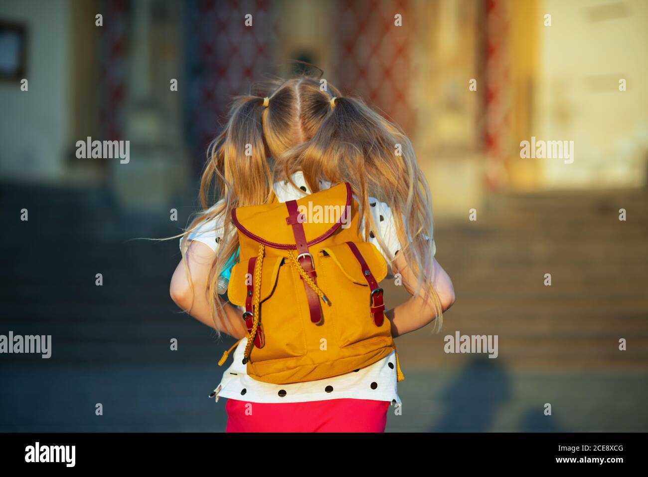 La vida durante la pandemia de covid-19. Visto desde detrás de la niña en blanco polka punto blusa con mochila amarilla yendo de la escuela fuera. Foto de stock