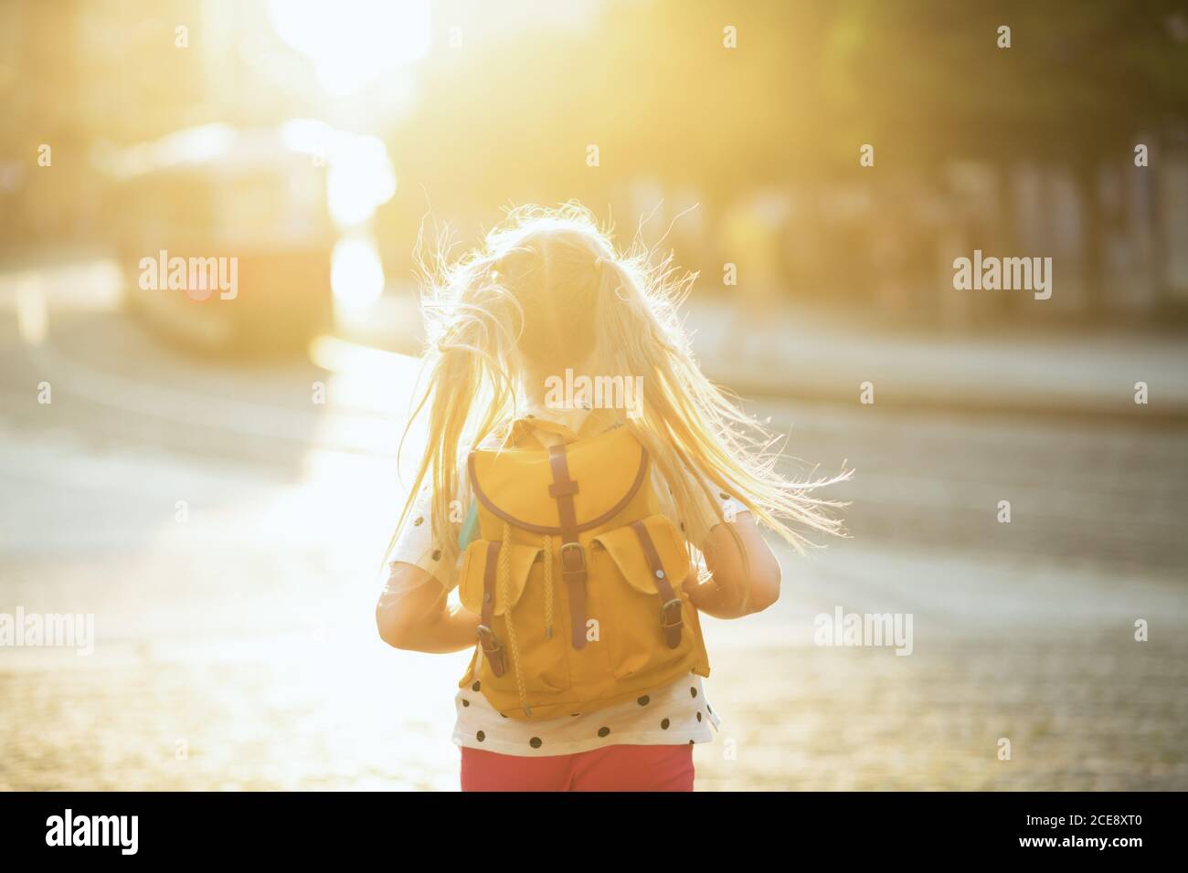 La vida durante la pandemia de covid-19. Visto desde detrás del niño en la blusa blanca de lunares con una mochila amarilla regresando de la escuela al aire libre. Foto de stock